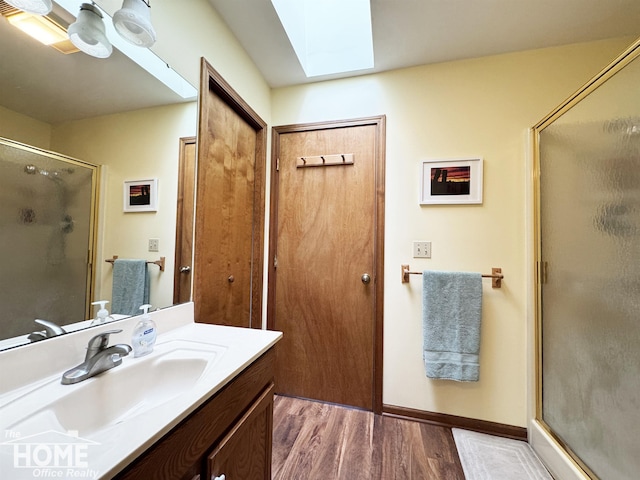 full bath with a skylight, a shower stall, vanity, wood finished floors, and baseboards