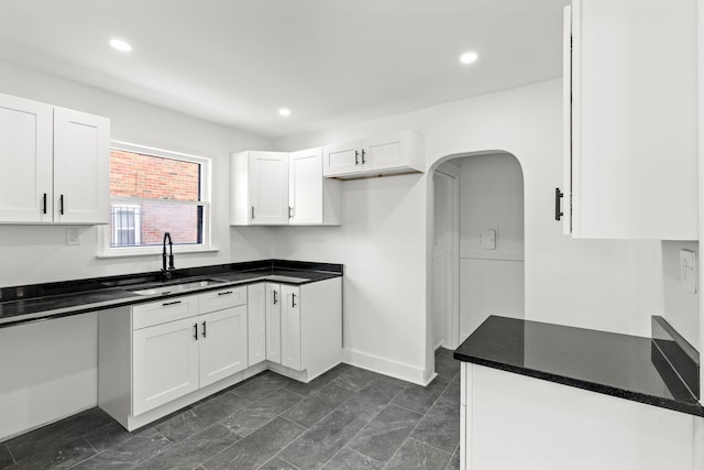 kitchen featuring arched walkways, baseboards, white cabinets, a sink, and recessed lighting