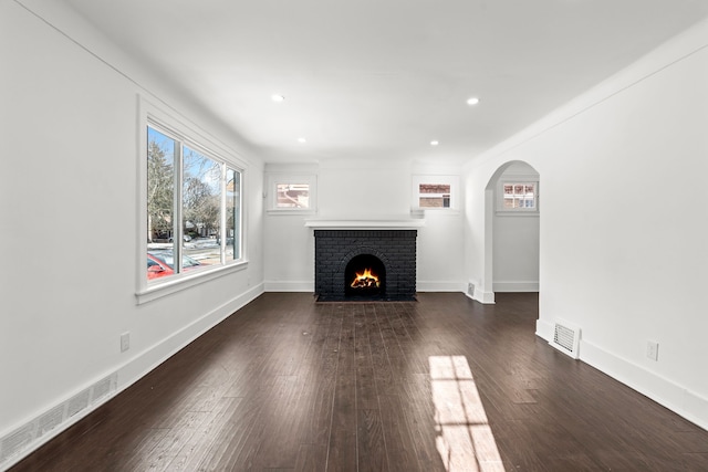 unfurnished living room featuring dark wood-style floors, arched walkways, visible vents, and baseboards