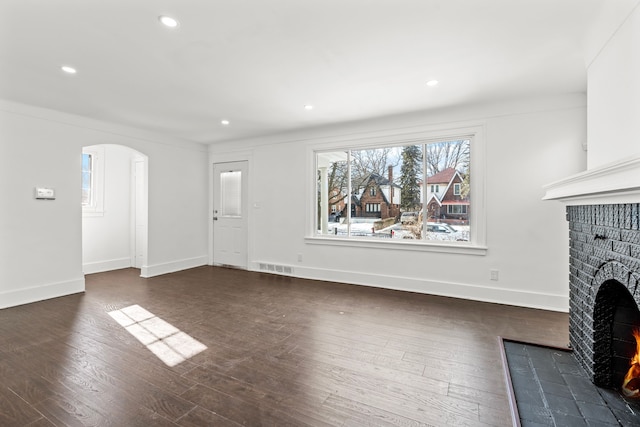 unfurnished living room with visible vents, arched walkways, baseboards, dark wood-type flooring, and a brick fireplace