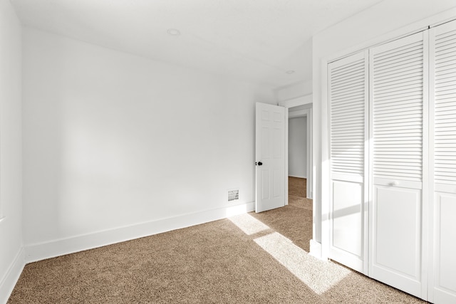 unfurnished bedroom with a closet, visible vents, light carpet, and baseboards