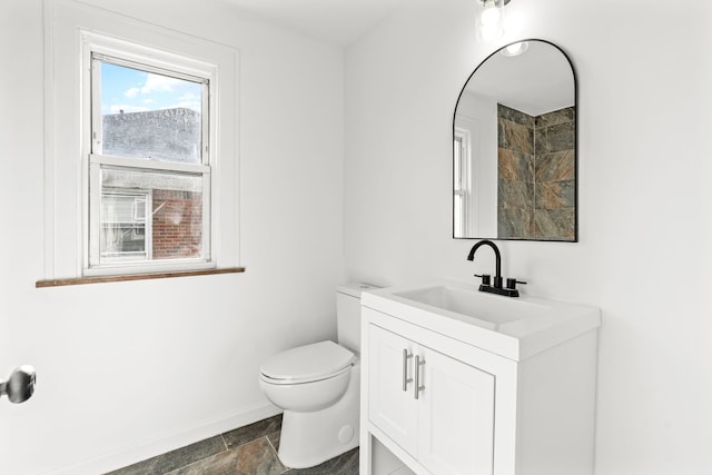 bathroom with stone finish flooring, baseboards, vanity, and toilet