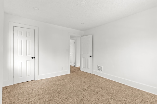 unfurnished room with a textured ceiling, carpet flooring, visible vents, and baseboards