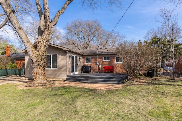 rear view of house with brick siding, a yard, and fence