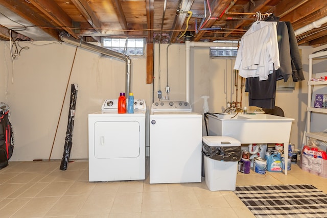 clothes washing area featuring washer and dryer, light tile patterned floors, laundry area, and a sink