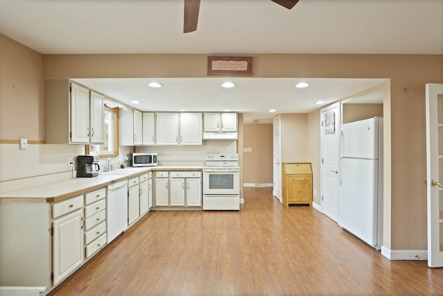 kitchen featuring light wood-type flooring, a sink, under cabinet range hood, white appliances, and light countertops