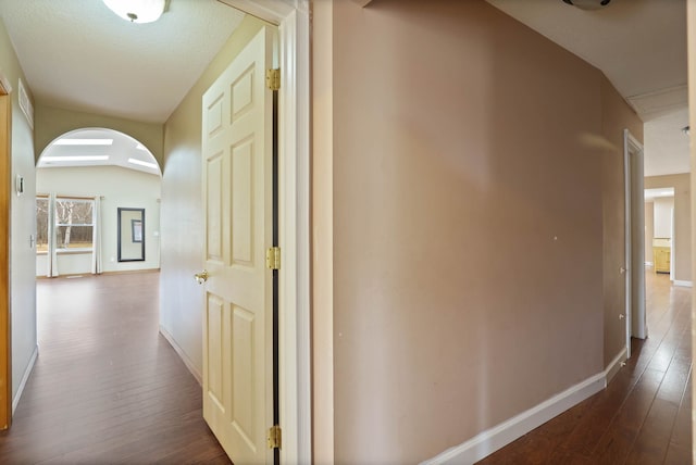 corridor featuring baseboards, arched walkways, and dark wood-style flooring