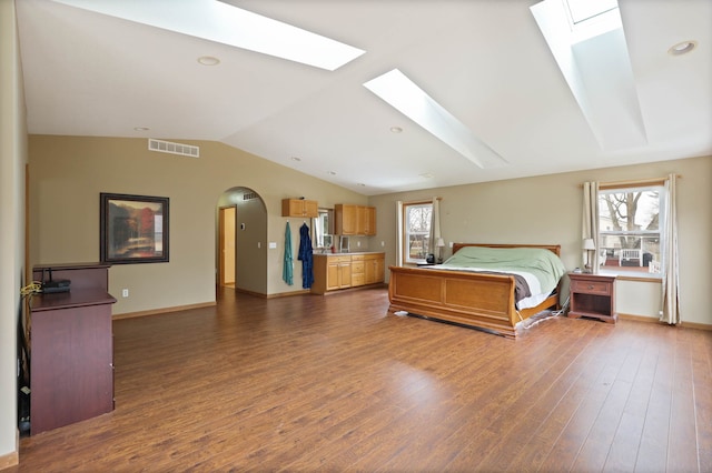 bedroom featuring wood finished floors, visible vents, vaulted ceiling with skylight, arched walkways, and multiple windows