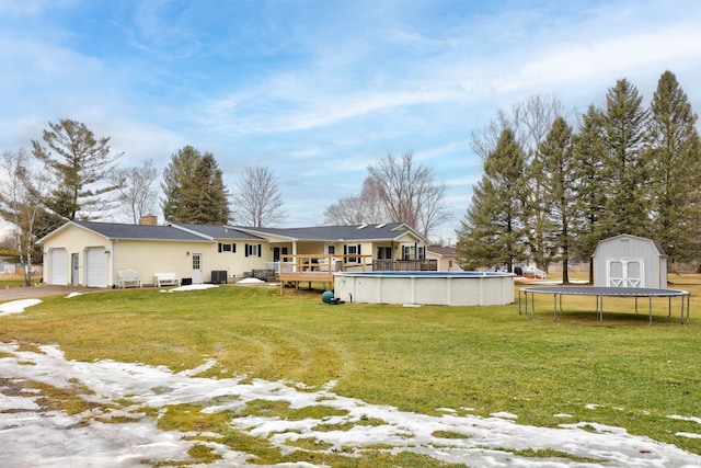 rear view of house with a yard, an attached garage, an outdoor pool, an outdoor structure, and a storage shed