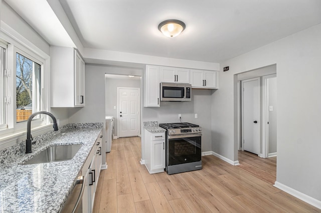 kitchen featuring light stone counters, light wood-style flooring, stainless steel appliances, white cabinetry, and a sink