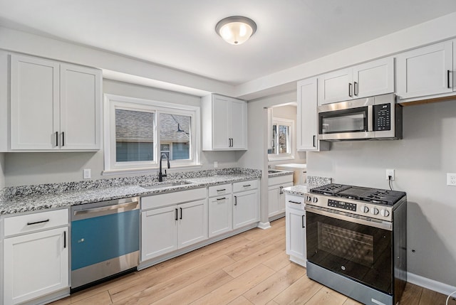 kitchen with light wood finished floors, light stone countertops, appliances with stainless steel finishes, and a sink