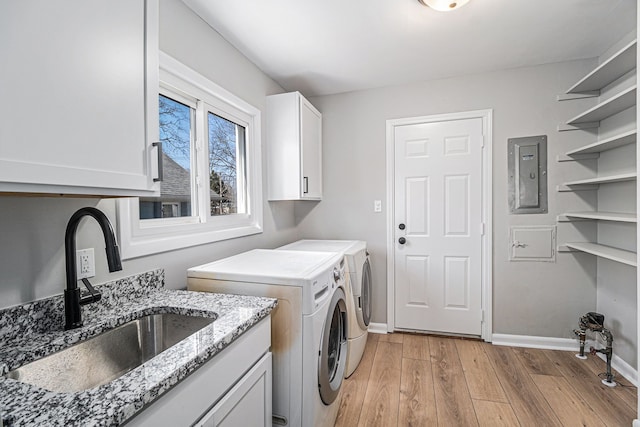 clothes washing area featuring a sink, electric panel, washing machine and dryer, cabinet space, and light wood-style floors