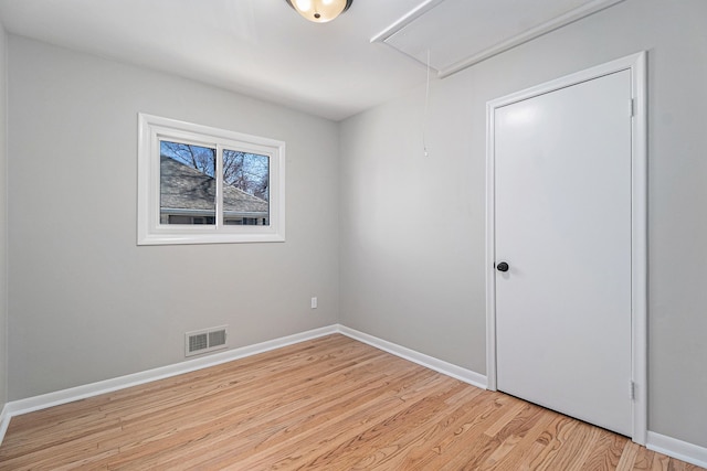 spare room with light wood-type flooring, visible vents, baseboards, and attic access