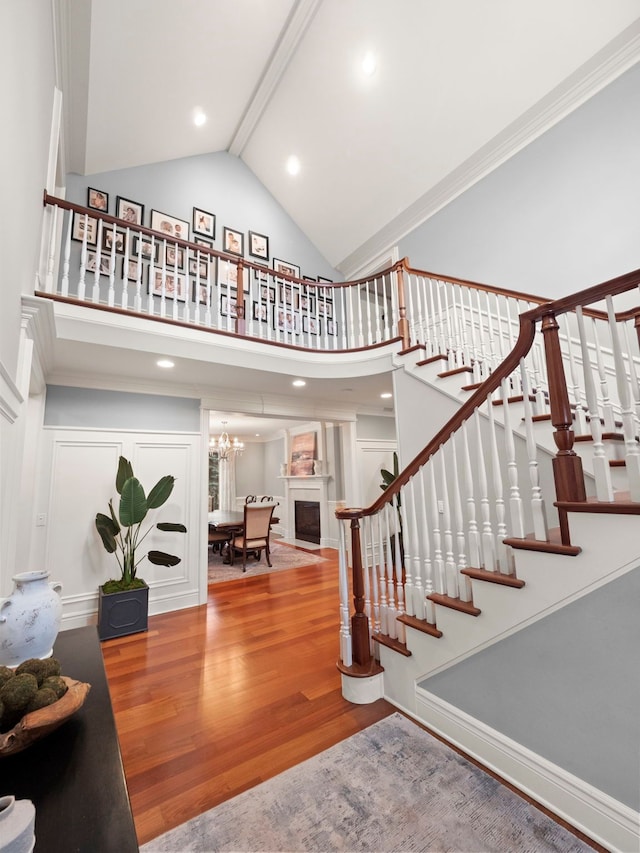 staircase with beamed ceiling, high vaulted ceiling, wood finished floors, an inviting chandelier, and a fireplace