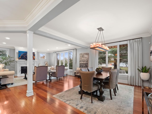 dining space with a fireplace, wood finished floors, ornate columns, and ornamental molding