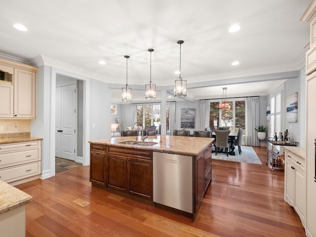 kitchen with wood finished floors, a kitchen island with sink, ornamental molding, a sink, and stainless steel dishwasher