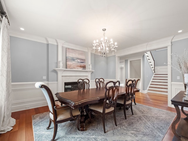 dining room featuring ornamental molding, a glass covered fireplace, wood finished floors, wainscoting, and stairs