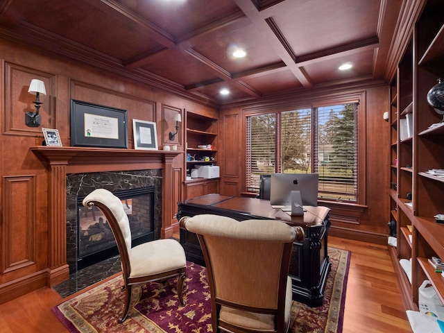 office area with built in shelves, wood walls, a premium fireplace, light wood-style flooring, and coffered ceiling