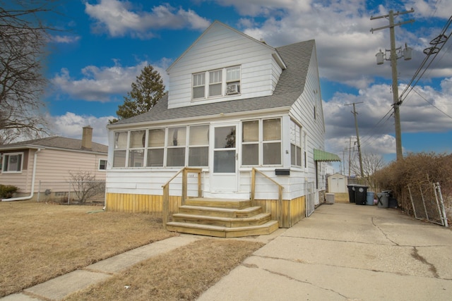 view of front of home featuring driveway, entry steps, a sunroom, roof with shingles, and an outbuilding