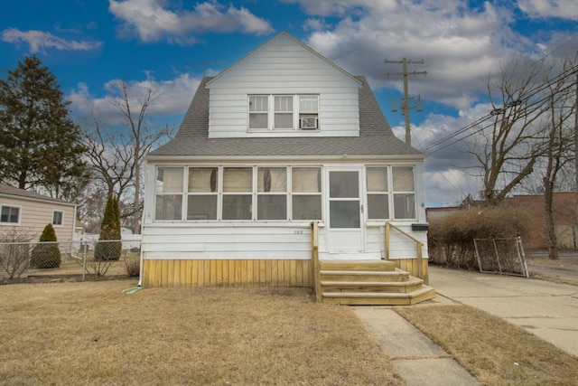 dutch colonial featuring a shingled roof, entry steps, a sunroom, fence, and a front lawn