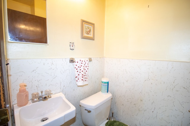 half bathroom featuring wainscoting, a sink, and toilet