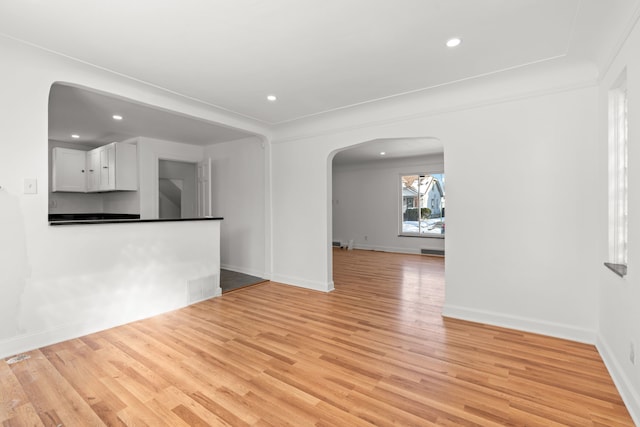 spare room with arched walkways, light wood finished floors, recessed lighting, and baseboards