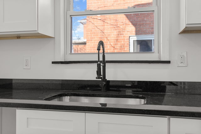 kitchen with dark countertops, white cabinetry, and a sink