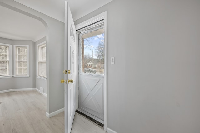 doorway to outside featuring arched walkways, light wood finished floors, visible vents, and baseboards