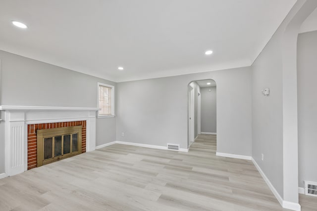 unfurnished living room featuring arched walkways, a fireplace, visible vents, wood finished floors, and baseboards