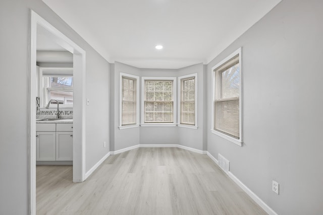 unfurnished dining area featuring light wood-style flooring, recessed lighting, a sink, visible vents, and baseboards