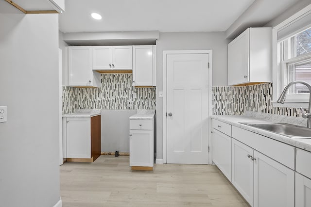 kitchen with light wood finished floors, light countertops, backsplash, white cabinets, and a sink