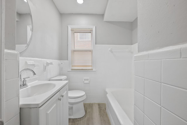 bathroom with toilet, a wainscoted wall, wood finished floors, a bathtub, and vanity