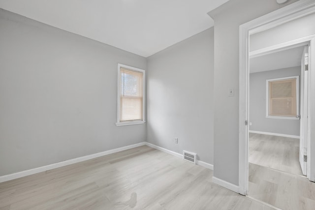 empty room with light wood-type flooring, visible vents, and baseboards