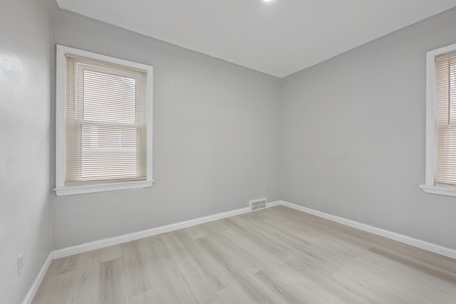 spare room featuring a wealth of natural light, visible vents, baseboards, and wood finished floors