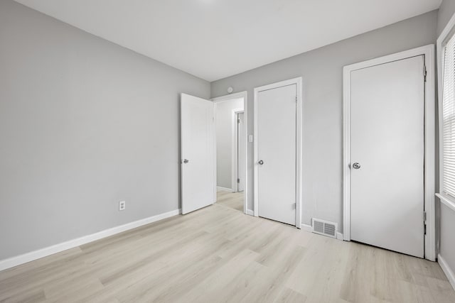 unfurnished bedroom with light wood-type flooring, visible vents, and baseboards