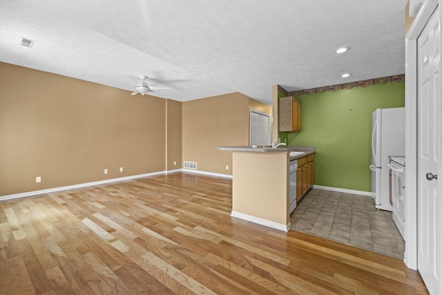 kitchen featuring a peninsula, light wood-style flooring, brown cabinetry, and visible vents