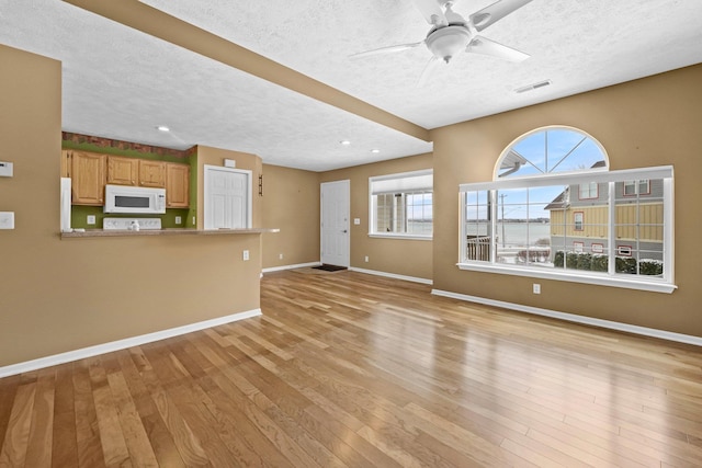 unfurnished living room with light wood-style floors, a textured ceiling, and baseboards