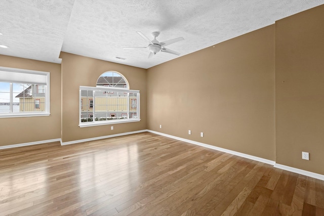 unfurnished room featuring plenty of natural light, wood finished floors, a ceiling fan, and baseboards