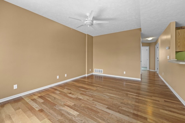 unfurnished room featuring ceiling fan, a textured ceiling, visible vents, baseboards, and light wood-type flooring