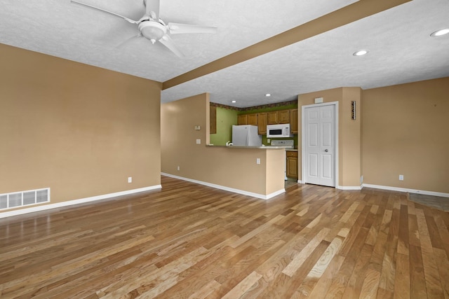 unfurnished living room with ceiling fan, light wood-style flooring, visible vents, and baseboards