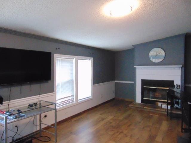 living area with a wainscoted wall, a textured ceiling, wood finished floors, and a glass covered fireplace