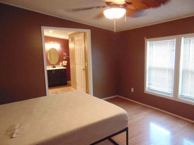 bedroom featuring baseboards, ensuite bath, light wood-style flooring, ornamental molding, and ceiling fan