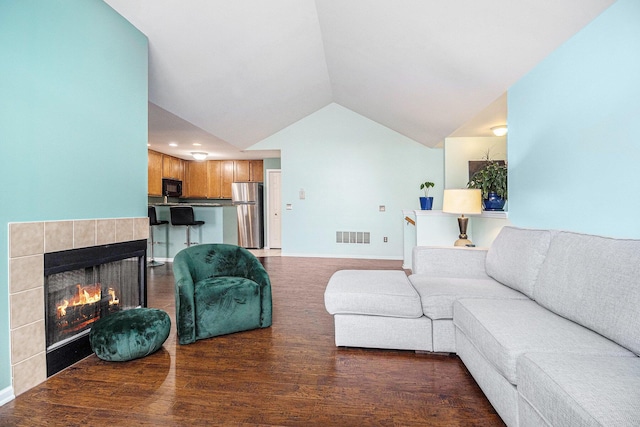 living area with a tile fireplace, visible vents, vaulted ceiling, and wood finished floors