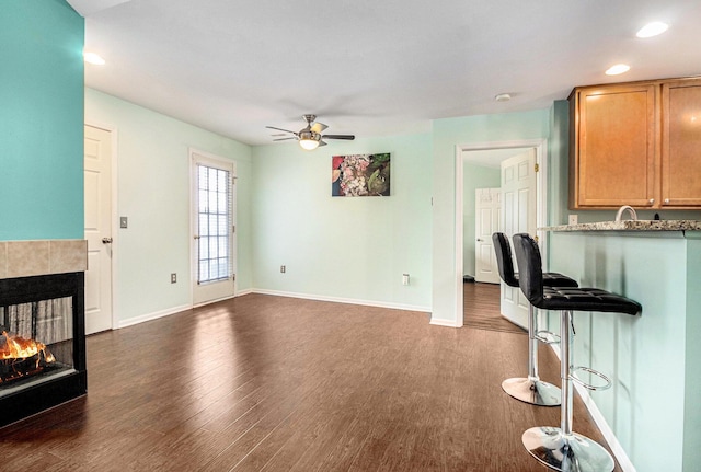 kitchen featuring dark wood-style floors, baseboards, a ceiling fan, and a tile fireplace