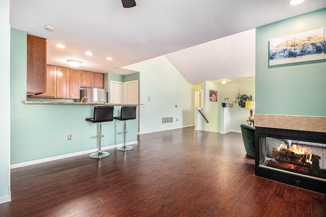 kitchen featuring dark wood finished floors, freestanding refrigerator, a peninsula, a kitchen bar, and a fireplace