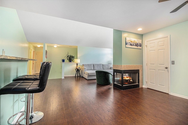 living room with baseboards, a ceiling fan, wood finished floors, and a multi sided fireplace