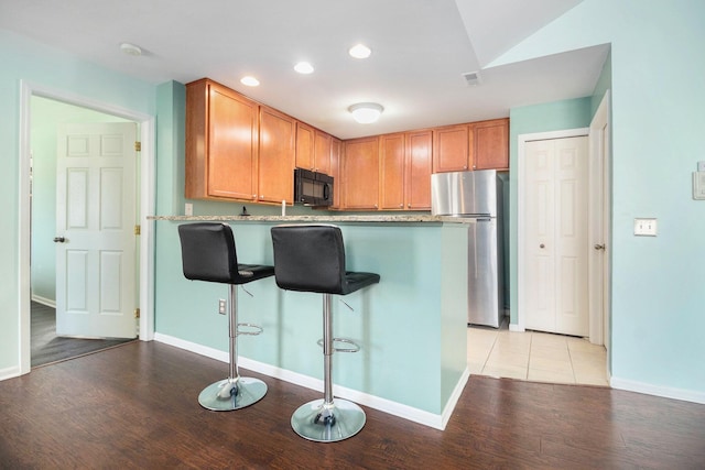 kitchen featuring freestanding refrigerator, black microwave, a peninsula, and light wood finished floors