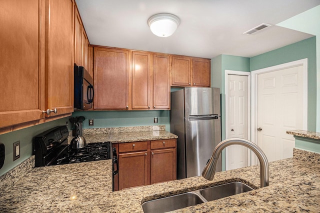 kitchen featuring black appliances, light stone counters, a sink, and visible vents