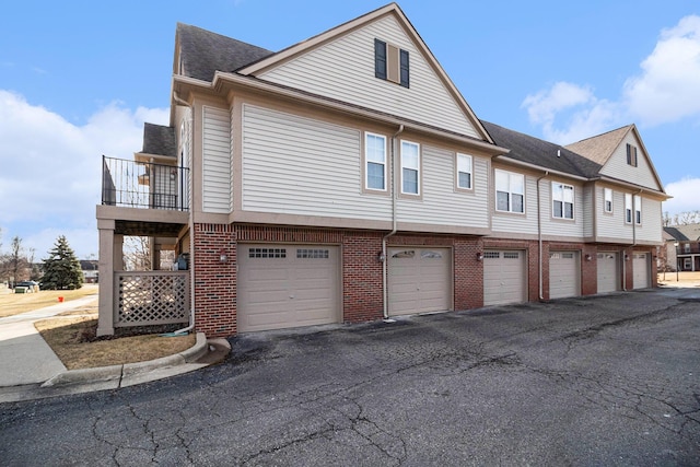 view of home's exterior featuring brick siding, a shingled roof, a balcony, and community garages