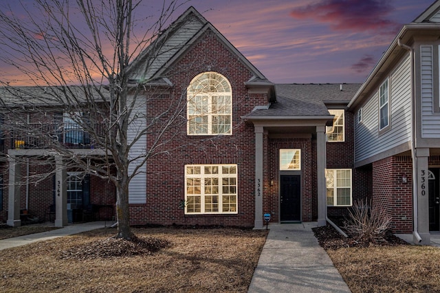 traditional home with roof with shingles and brick siding